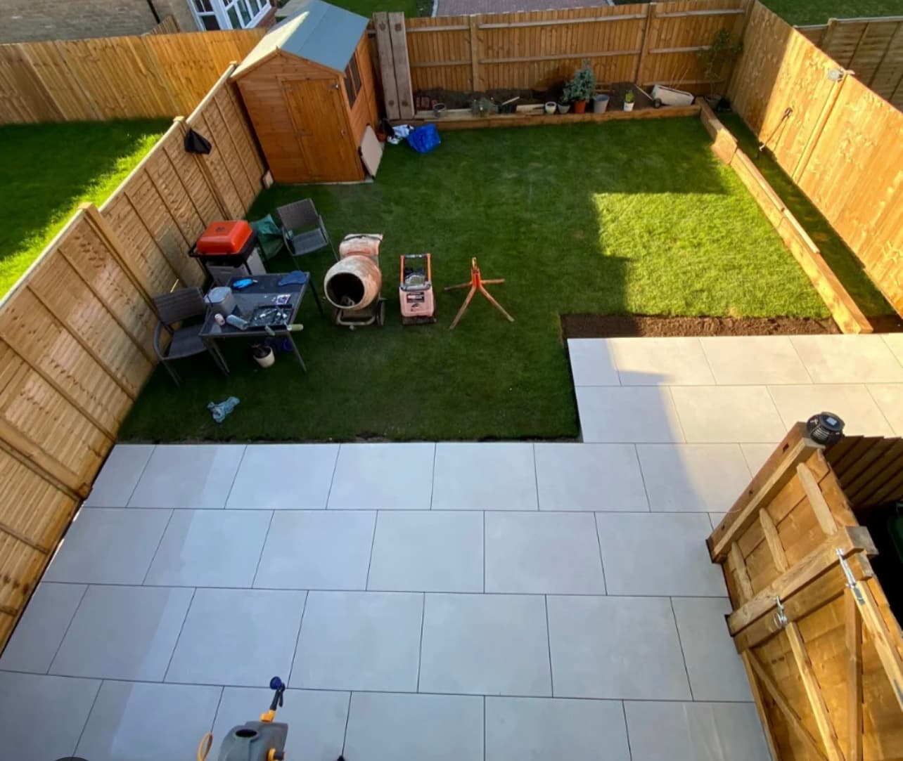Aerial view of L-shaped porcelain patio with fresh lawn and wooden fencing